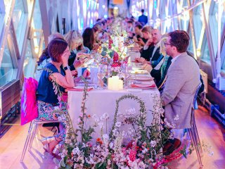 An evening event in the Walkways with a long trestle table set for dinner and people seated along both sides.  